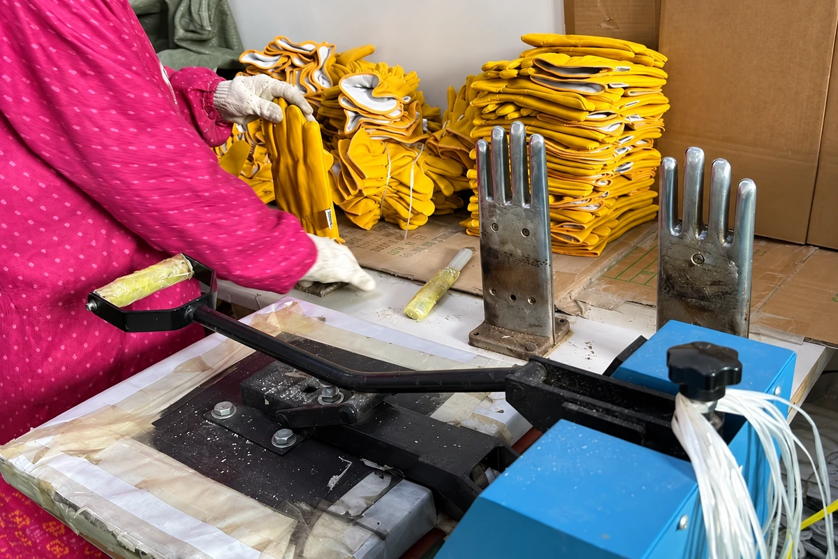 Worker handling yellow gloves beside metal hand forms