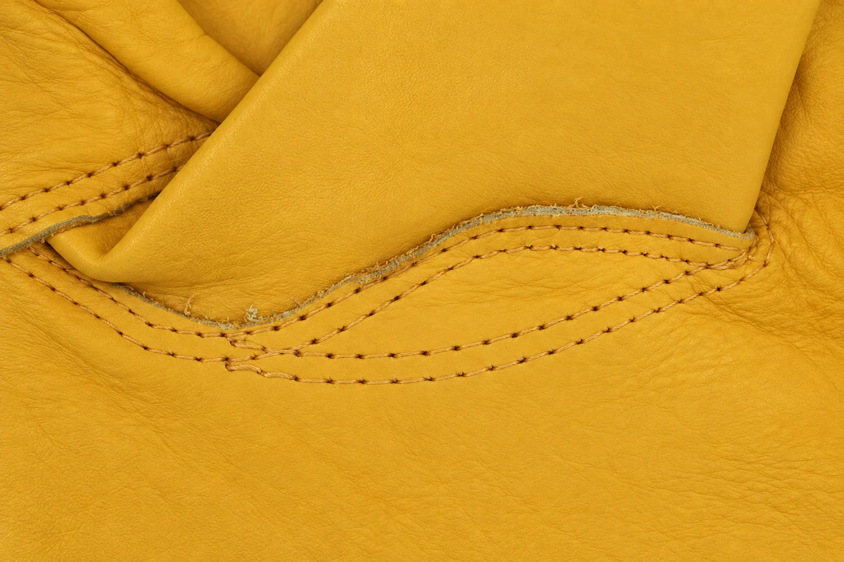 Yellow leather grain and double stitching around a glove thumb