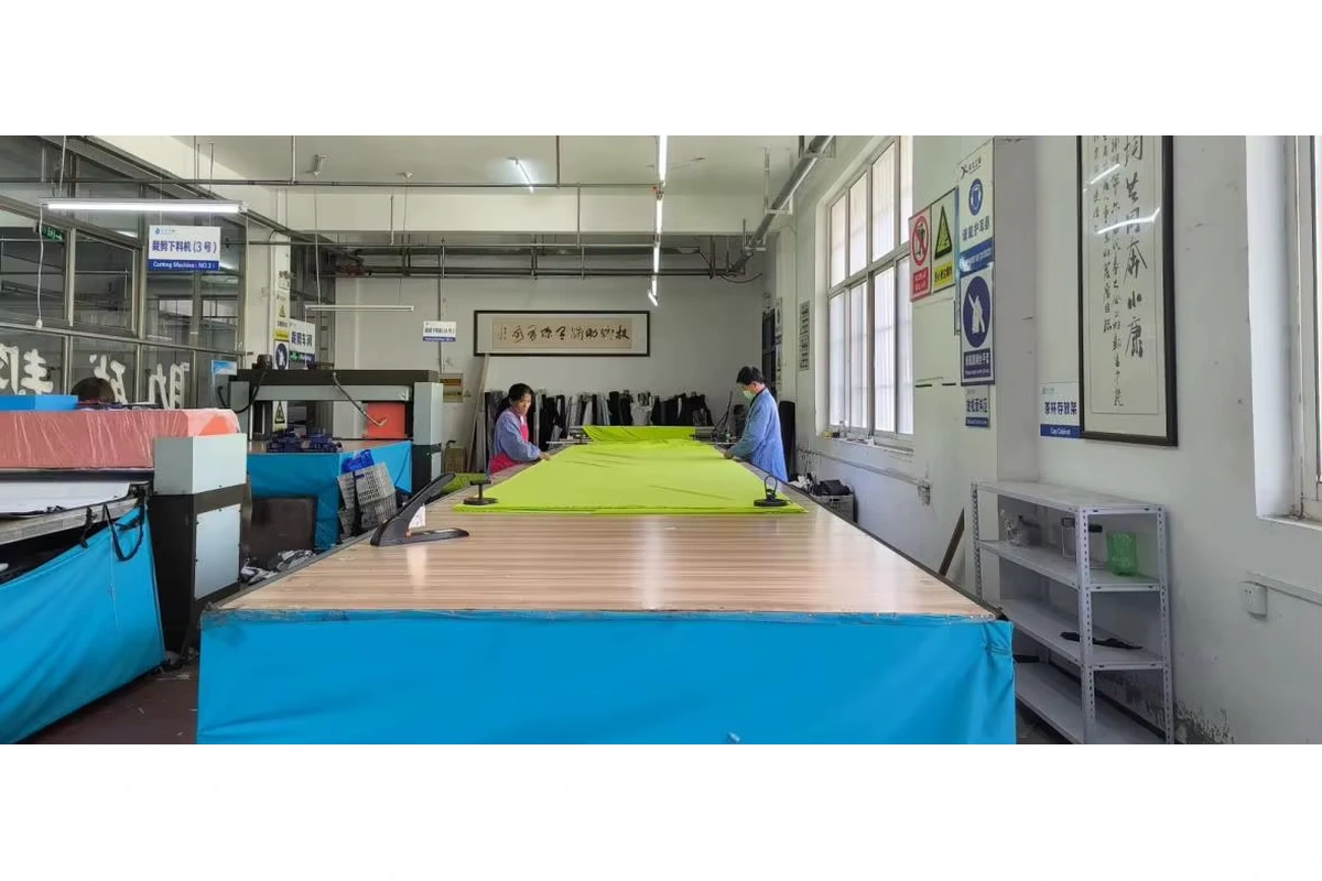 Workers preparing bright fabric on a long table near cutting equipment