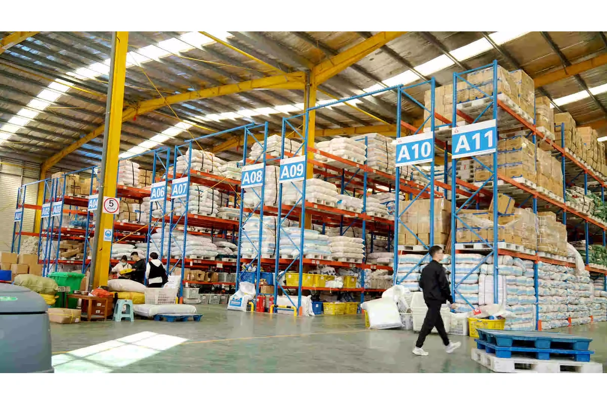 Warehouse racks holding wrapped bundles and cartons beside a packing area