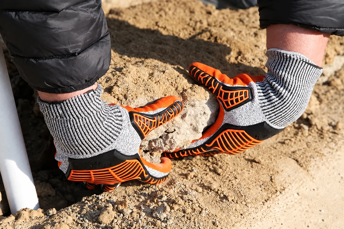 Orange and gray reinforced gloves lifting a stone
