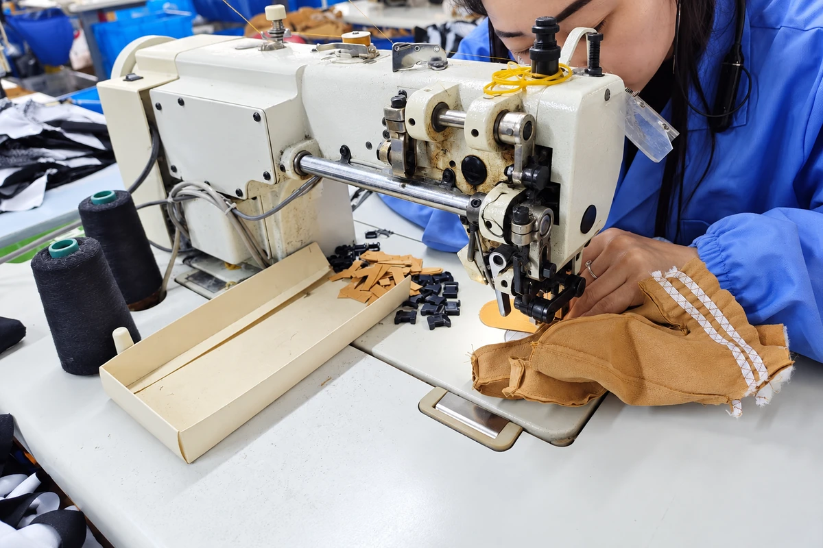 Worker stitching a tan leather glove at a sewing machine