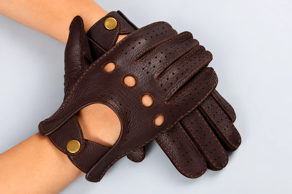 Brown perforated driving gloves worn with button wrist closures