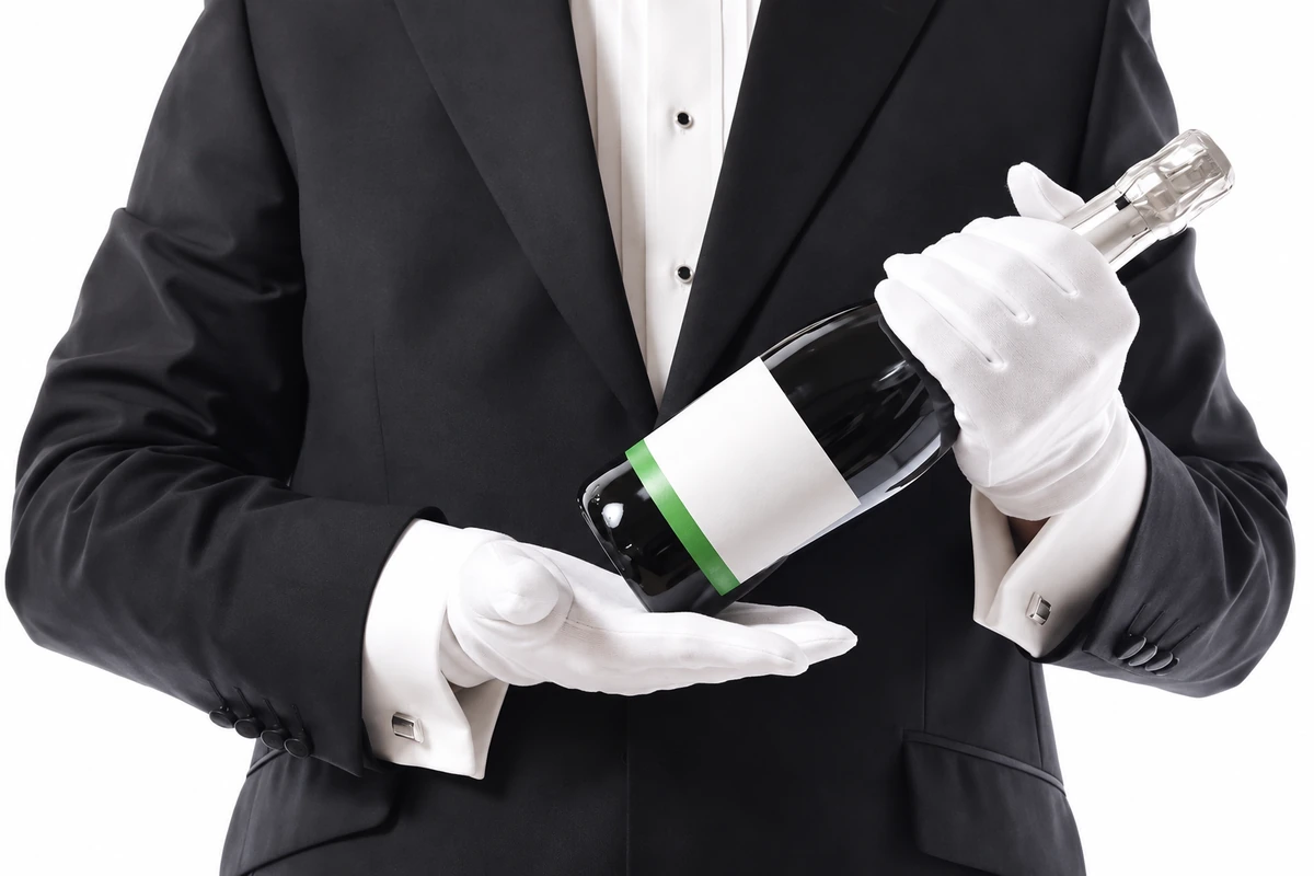 White gloves worn by a formally dressed person holding a bottle