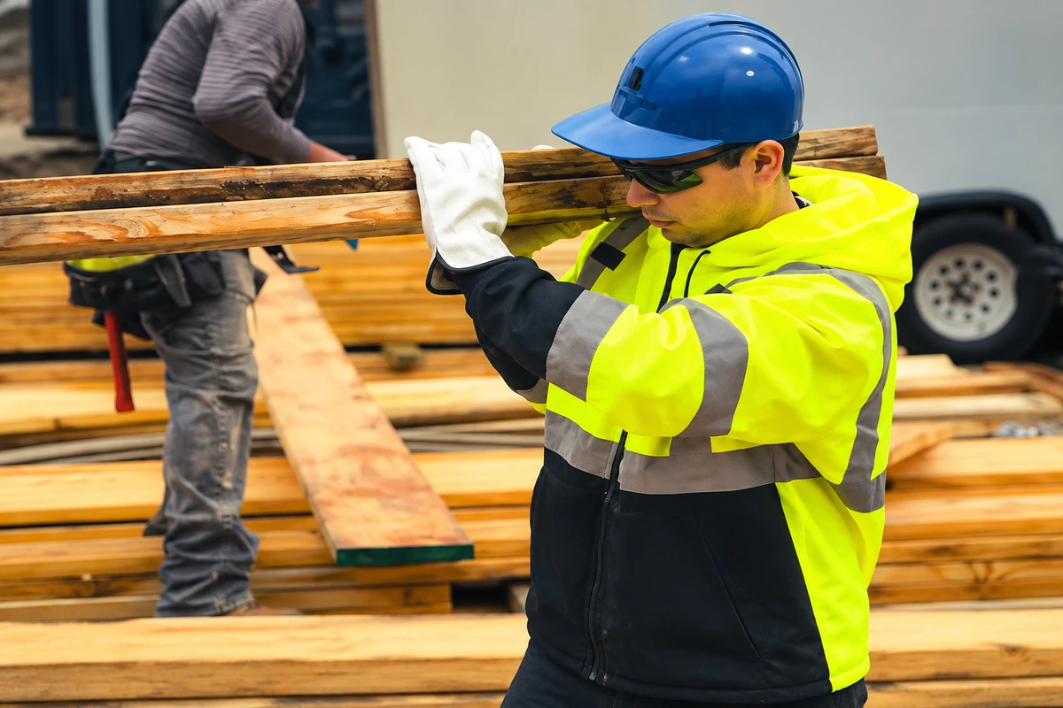Worker wearing white leather gloves while carrying timber