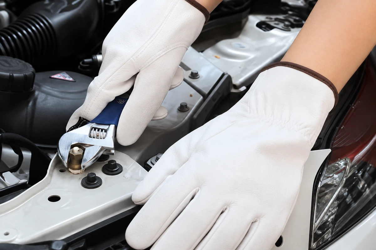 White leather gloves holding an adjustable wrench at a car engine