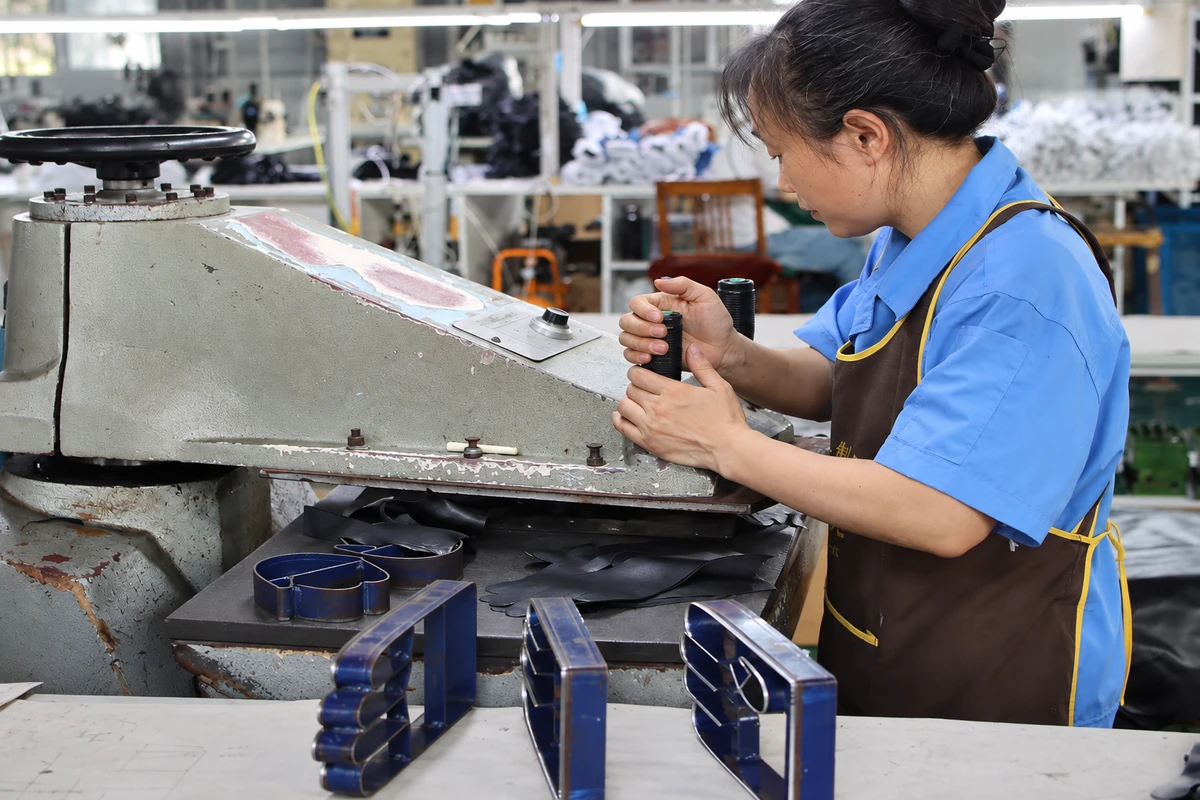Worker cutting black glove panels with a die-cutting press