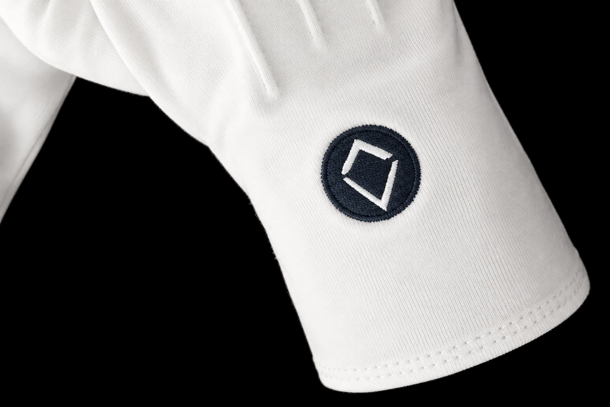 Close view of a dark circular embroidered emblem on a white glove cuff