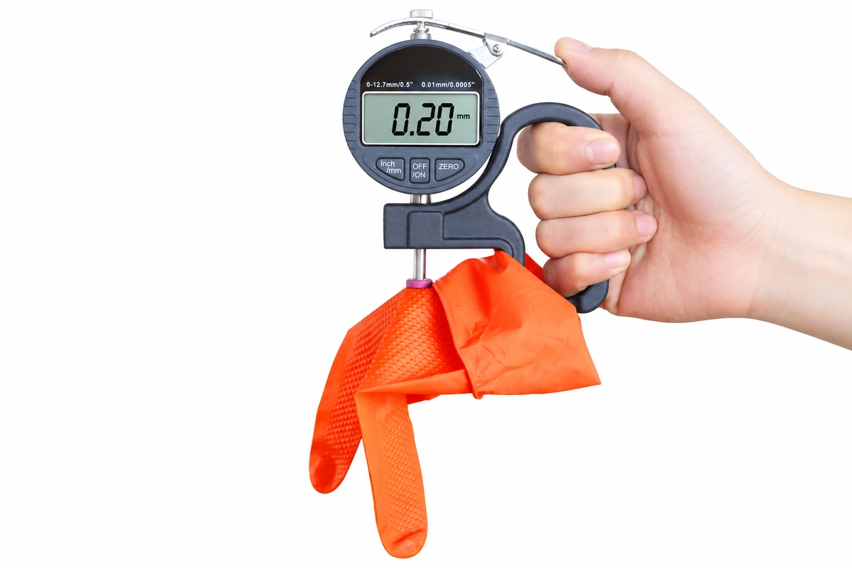Thickness gauge contacting an orange disposable glove sample