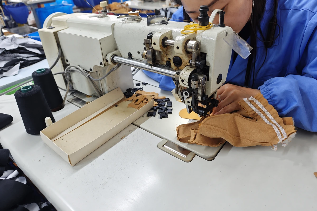 Operator sewing a tan glove on an industrial machine