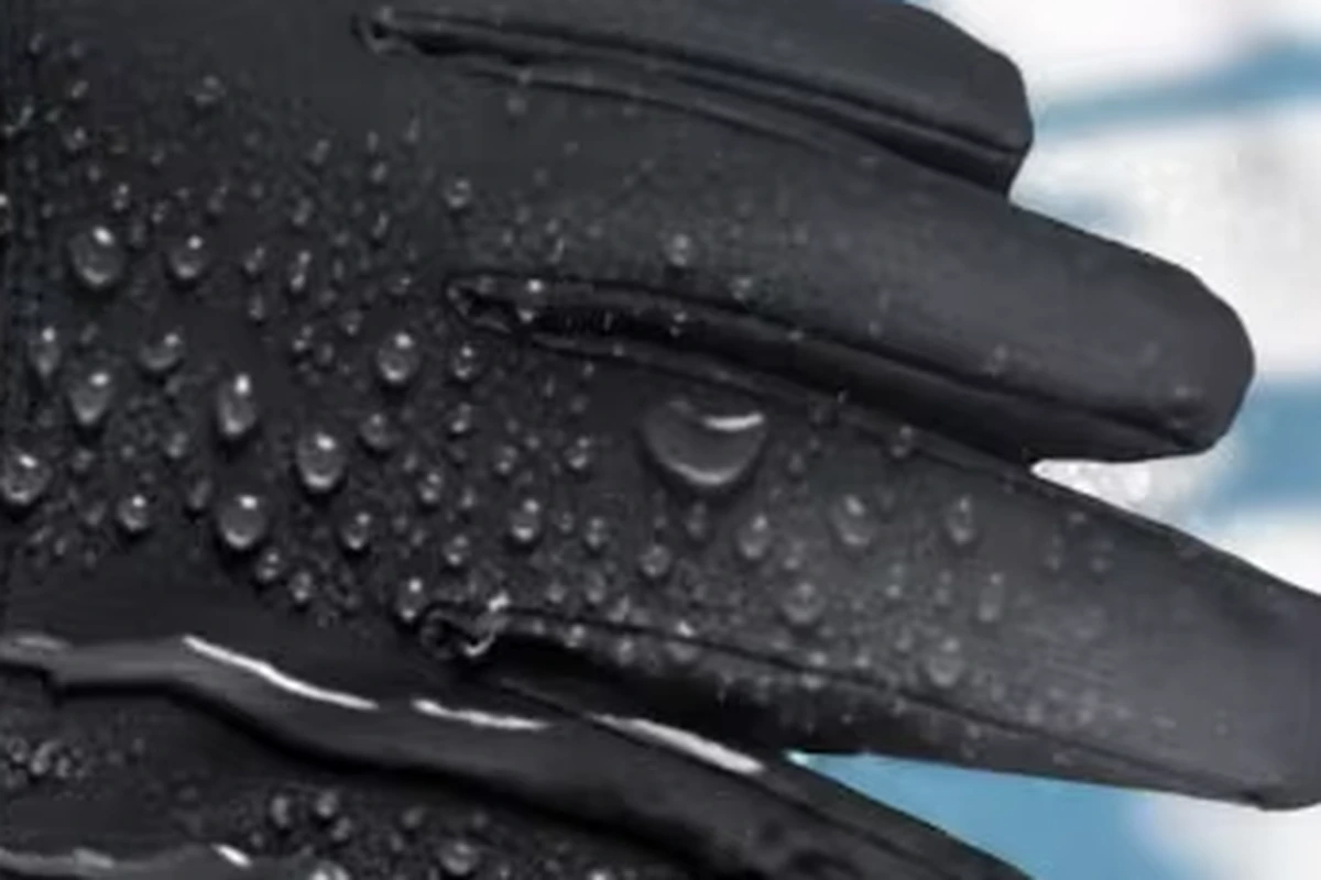 Water droplets on the dark fabric and fingers of a winter glove